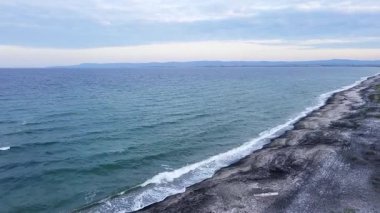 Deep calm undulating Black Sea with foamy sea waves and turquoise transparent cool water washing a sandy empty wild coast with grains of black sand, under a cloudy gray sky. UHD 4K video realtime