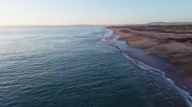 Sakin mavi uçsuz bucaksız Karadeniz, ışığı yansıtan soğuk su ve yakındaki kumlu boş kumsal, bulutlu renkli gökyüzüne karşı beyaz bulutlar ve parlak şafak güneşi. UHD 4K video gerçek zamanlı