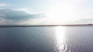 Boundless calm Black Sea with cool water reflecting light extends beyond the horizon, under colored sky with white volatile clouds and a bright dawn warm spring sun. UHD 4K video realtime