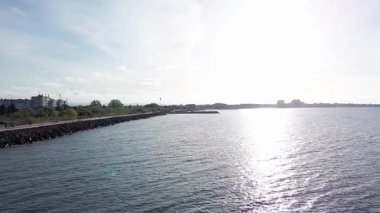 Sea promenade with people walking near the deep calm cool Black Sea, against the backdrop of the ancient resort small town of Pomorie in Bulgaria under a cloudy soft blue sky. UHD 4K video realtime