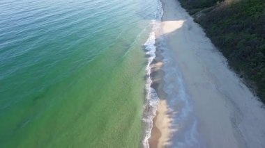 A wild empty sandy beach between a rocky sharp large ledge, covered with green fresh new vegetation, and a deep calm cool Black Sea under a clear blue sky. UHD 4K video realtime