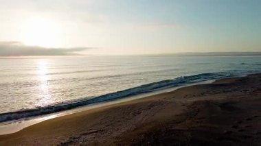 Sakin mavi uçsuz bucaksız Karadeniz, ışığı yansıtan soğuk su ve yakındaki kumlu boş kumsal, bulutlu renkli gökyüzüne karşı beyaz bulutlar ve parlak şafak güneşi. UHD 4K video gerçek zamanlı