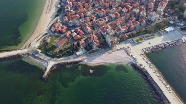 Küçük, yeni inşa edilmiş bir tatil köyünün kuş bakışı manzarası - Pomorie yarımadası, büyük, tuzlu, sakin Karadeniz 'de birçok farklı modern tekne ve tekne. UHD 4K video gerçek zamanlı