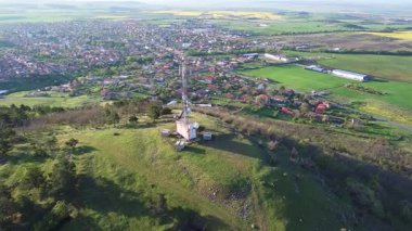 Parlak geniş çiçek tarlaları, dağda küçük bir bitki ve çayır vadisinde küçük boş bir köy ve bulutlu mavi gökyüzü. UHD 4K video gerçek zamanlı