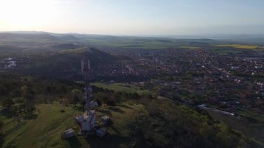 Parlak geniş çiçek tarlaları, dağda küçük bir bitki ve çayır vadisinde küçük boş bir köy ve bulutlu mavi gökyüzü. UHD 4K video gerçek zamanlı