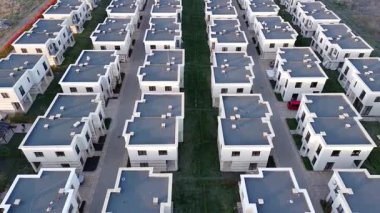 Birds eye view panorama of a large number of small gray resort identical apartments in a small town with empty streets and modern cars, surrounded by green meadows and fields. UHD 4K video realtime