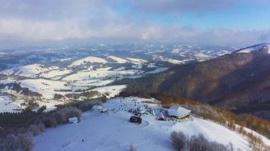 Yoğun yeşil ormanlarla kaplı dik bir dağ yamacında eski bir kayak istasyonu. Bir sürü sıcak giyimli insan kayak ve snowboard yapıyor.