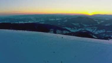 Karpatlar 'ın olağanüstü vadisi, karla kaplı tepeler ve dağlarla kaplı sonsuz yeşil ladin ormanlarıyla sıcak, parlak günbatımının arka planına karşı.