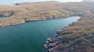 Bulgaristan 'ın parlak güneşli akşam günbatımına karşı sakin, mavi yansıtıcı Karadeniz ve eski karanlık kayalık taşlarla kaplı deniz manzarası. UHD 4K video gerçek zamanlı