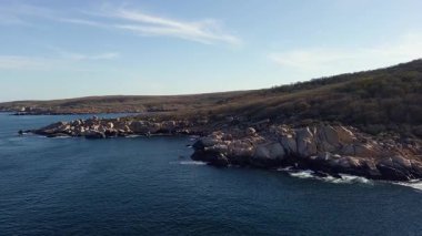 Bulgaristan 'ın parlak güneşli akşam günbatımına karşı sakin, mavi yansıtıcı Karadeniz ve eski karanlık kayalık taşlarla kaplı deniz manzarası. UHD 4K video gerçek zamanlı