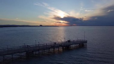 Bulgaristan 'ın Pomorie kentinde, bulutlu, çok renkli bir gökyüzü ve parlak bir akşam batımına karşı sakin ve sakin bir Karadeniz' deki eski, boş, küçük bir rıhtımın yan görüntüsü. UHD 4K video gerçek zamanlı