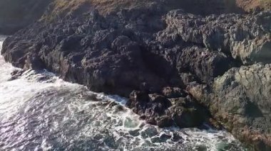 Bulgaristan 'ın parlak güneşli akşam günbatımına karşı sakin, mavi yansıtıcı Karadeniz ve eski karanlık kayalık taşlarla kaplı deniz manzarası. UHD 4K video gerçek zamanlı