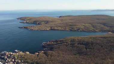 Bulgaristan 'ın parlak güneşli akşam günbatımına karşı sakin, mavi yansıtıcı Karadeniz ve eski karanlık kayalık taşlarla kaplı deniz manzarası. UHD 4K video gerçek zamanlı