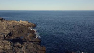 Bulgaristan 'ın parlak güneşli akşam günbatımına karşı sakin, mavi yansıtıcı Karadeniz ve eski karanlık kayalık taşlarla kaplı deniz manzarası. UHD 4K video gerçek zamanlı