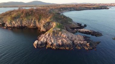 Bulgaristan 'ın açık mavi gökyüzü altında, sessiz turkuaz şeffaf Karadeniz ile çevrili, yabani çimenler ve otellerle kaplı kayalık kumlu dar sahillerin yükseklik ve yanından manzaraya bak. UHD 4K video gerçek zamanlı