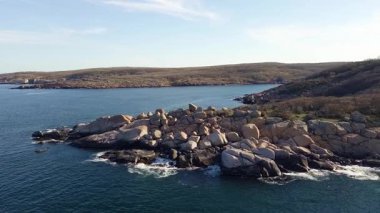 Bulgaristan 'ın parlak güneşli akşam günbatımına karşı sakin, mavi yansıtıcı Karadeniz ve eski karanlık kayalık taşlarla kaplı deniz manzarası. UHD 4K video gerçek zamanlı