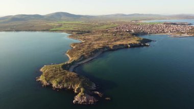Bulgaristan 'ın açık mavi gökyüzü altında, sessiz turkuaz şeffaf Karadeniz ile çevrili, yabani çimenler ve otellerle kaplı kayalık kumlu dar sahillerin yükseklik ve yanından manzaraya bak. UHD 4K video gerçek zamanlı