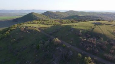Birds eye view of spring blooming green meadows and wooded hilly slopes of the Balkan Mountains, under the light of a bright cloudy warm day in the country of Bulgaria. UHD 4K video realtime