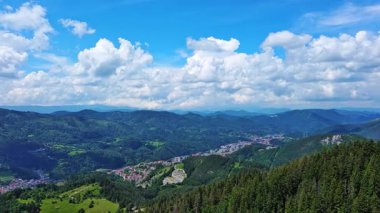 View from high rock to old village town Smolyan with green meadows for cattle walking and houses, between mountain range of Rhodope Mountains sheltered by spruce forests. UHD 4K video realtime