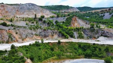 Industrial quarry for extraction of minerals with equipment and machines, and intermountain winding road passing by, in Rhodope Mountains covered with coniferous forests. UHD 4K video realtime