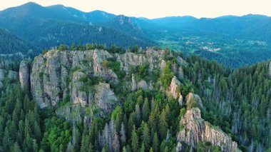 High rocky wild mountain range of Rhodope Mountains covered with green vegetation, against backdrop of mountain valley covered with dense dark spruce forests and blue cloudy sky. UHD 4K video realtime