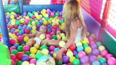 Neşeli, güzel, zeki ablası, tatlı küçük erkek kardeşiyle oynuyor ve küçük bir oyun odasında otururken ona renkli küçük toplar atıyor. 4K UHD yavaş çekim videosu