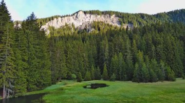 Işıl ışıl parlayan berrak göl, berrak mavi bulutlu bir gökyüzüne, yeşil ağaçlık dağ sıralarına ve küçük çiftçi dağ köylerine karşı parlak sıcak güneş ışığını yansıtır. UHD 4K video gerçek zamanlı