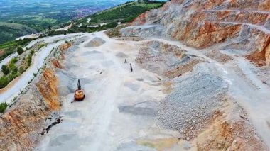 A natural stepped quarry rich in minerals is located near winding road, against backdrop of Rhodope Mountains and hills with evergreen spruce forests and mountain vegetation. UHD 4K video realtime