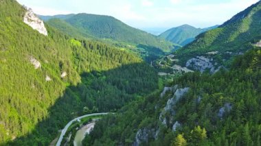 Dar, dolambaçlı bir dağ yolu, Rodop Dağları 'ndaki mavi bulutlu bir gökyüzünün altında yeşil yay dağ bitkilerinin bulunduğu dağ kanyonlarından geçer. UHD 4K video gerçek zamanlı