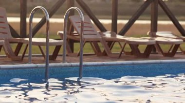 Sıcak, parlak bir günbatımının arka planına karşı yaz tatilinde, şeffaf, küçük ışık dalgaları ile serin, derin bir havuzun üst görüntüsü. 4K UHD yavaş çekim videosu