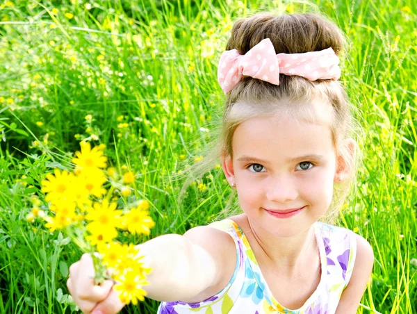 Bedårande leende liten flicka på ängen med blommor — Stockfoto