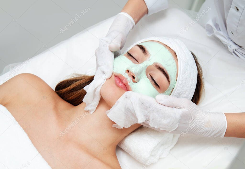 Young woman getting facial beauty treatment. Beautician cleaning and touching female face after facial mask. Attractive girl is lying and relaxing. Skin care and rejuvenation concept