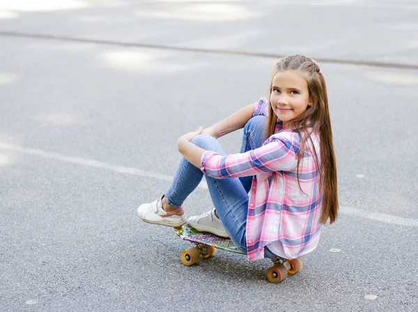 スケートボードに座ってかわいい女の子の子供を笑顔 屋外で夏の日にペニーボードでプレティーン — ストック写真