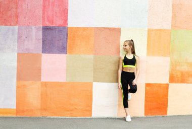 Spor kıyafetleriyle spor yapan genç bir kız duvarda yoga egzersizi yapıyor. Açık havada spor jimnastikçisi çocuk eğitimi. Sağlıklı yaşam tarzı ve vücut bakımı kavramı