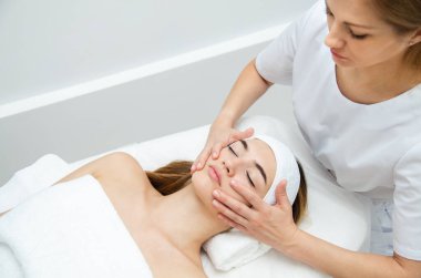 Güzellik uzmanı kadının yüzüne masaj yapıyor. Çekici kız yüz bakımı ve masaj yaptırıyor. Genç kadın yalan söylüyor ve dinleniyor..