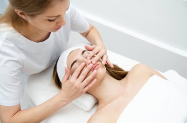 Güzellik uzmanı kadının yüzüne masaj yapıyor. Çekici kız yüz bakımı ve masaj yaptırıyor. Genç kadın yalan söylüyor ve dinleniyor..