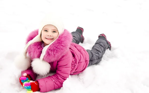 Cute smiling little girl lying on snow in winter day — Stock Photo, Image