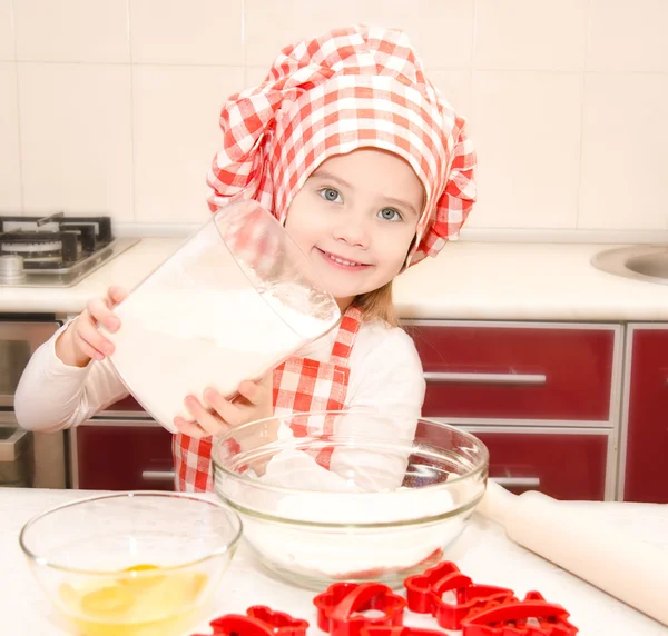 Улыбающаяся маленькая девочка в шляпе шеф-повара положила муку для выпечки печенья — стоковое фото