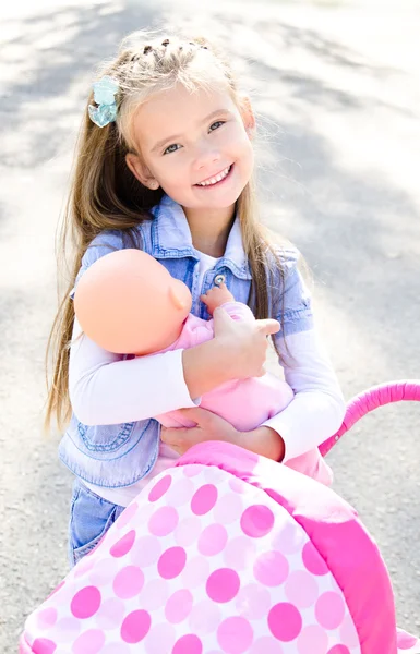 Милая улыбающаяся маленькая девочка, играющая со своей игрушечной каретой — стоковое фото