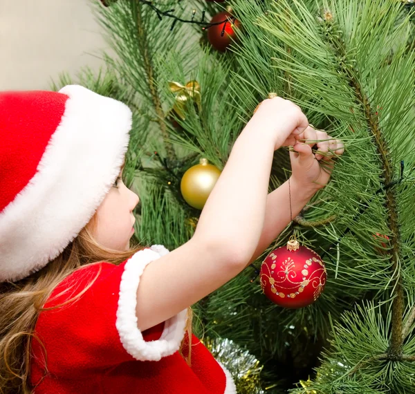 Маленькая девочка в шляпе Санты украшает рождественскую елку — стоковое фото
