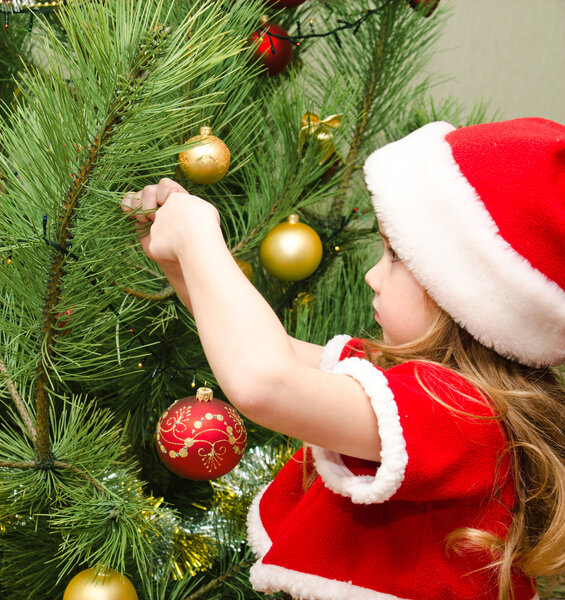 Little girl in santa hat decorating the christmas tree 