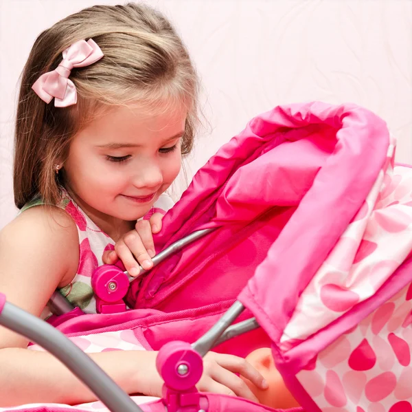 Cute smiling little girl playing with her toy carriage — Stock Photo, Image