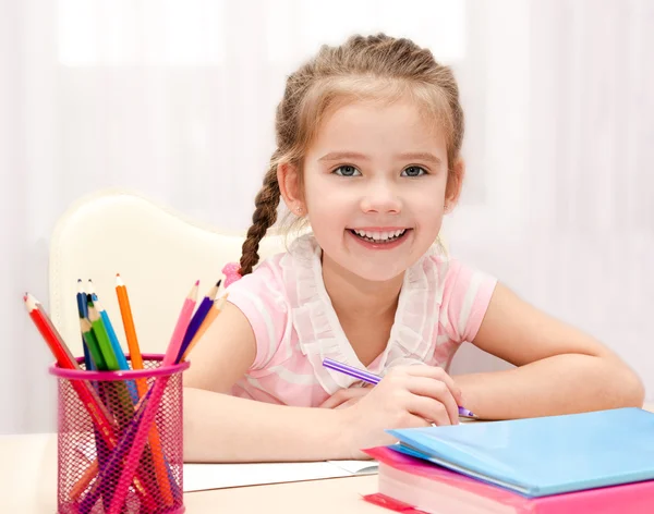 Carino sorridente bambina sta scrivendo alla scrivania — Foto Stock