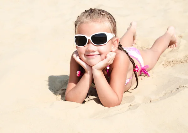 Happy cute little girl in sunglasses lying on the sand — Stock Photo, Image