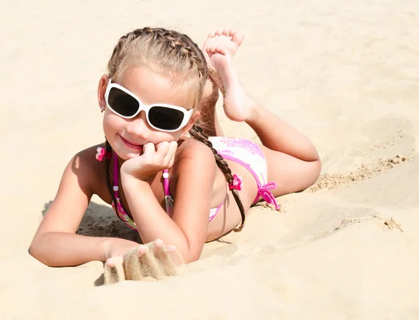 Happy cute little girl in sunglasses lying on the sand — Stock Photo, Image