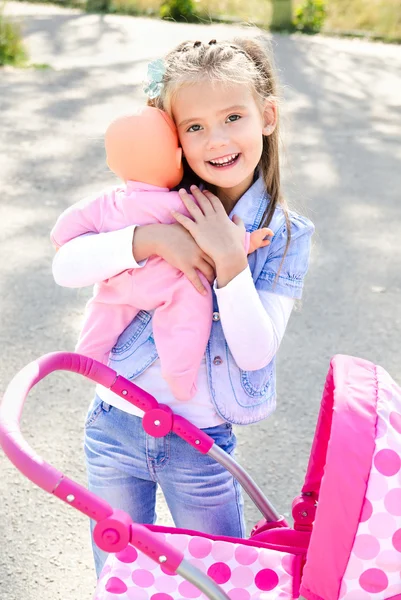 Roztomilá usměvavá holčička hraje s její hračka kočárek — Stock fotografie