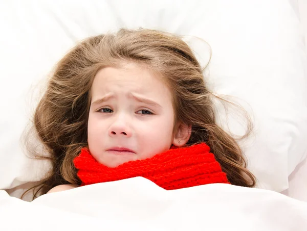 Sick little girl lying in the bed in red scarf — Stock Photo, Image