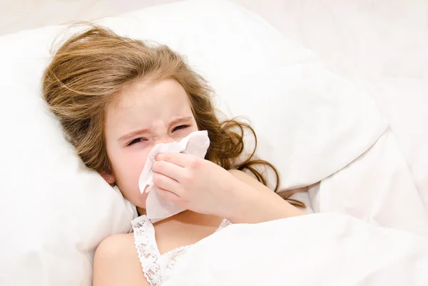 Little girl lying in the bed blowing her nose — Stock Photo, Image