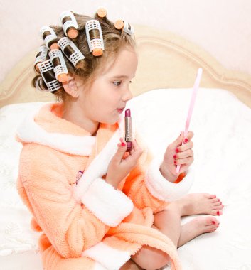 Little girl with lipstick and mirror and hair curlers
