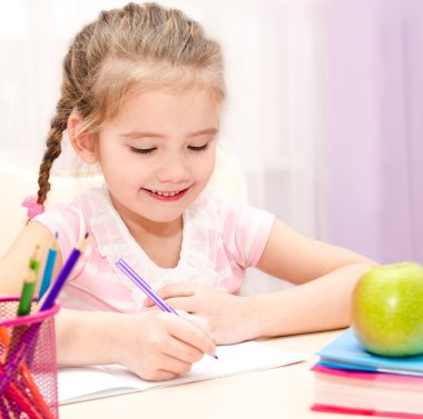 Cute little girl is writing at the desk clipart